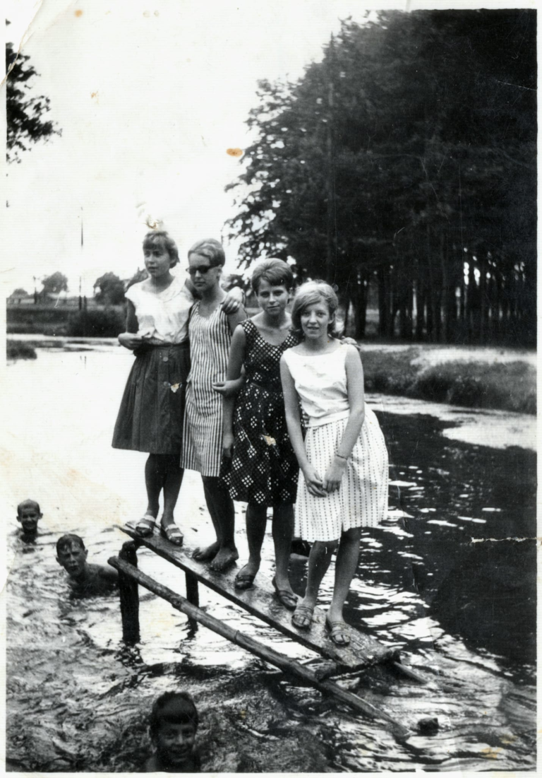 Cztery panie (p. Urszula Zarębska , p. Irena Miazga , p. Związkiewicz i p. Zdanowska) pozują do zdjęcia nad Stawem Traczewskim. Obok nich w wodzie kąpie się kilku chłopców.
