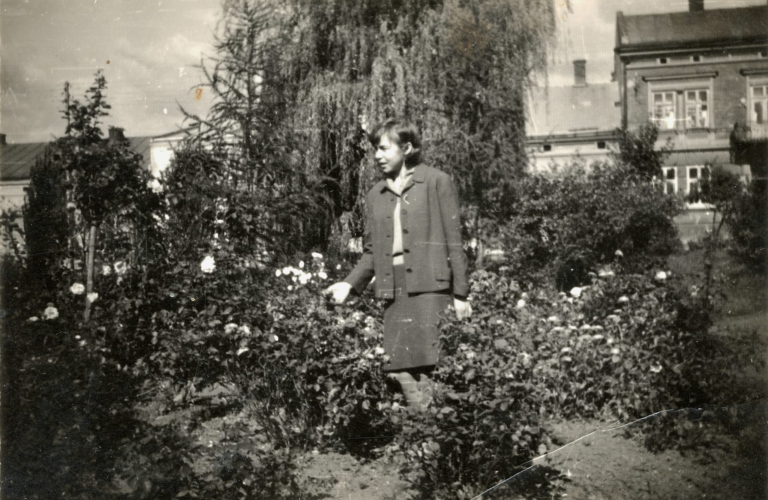 Pani Irena Miazga pozuje do zdjęcia na plantach w północno – wschodniej części Rynku w Głogowie. W tle widoczne kamienice w Rynku nr 19 – 23.