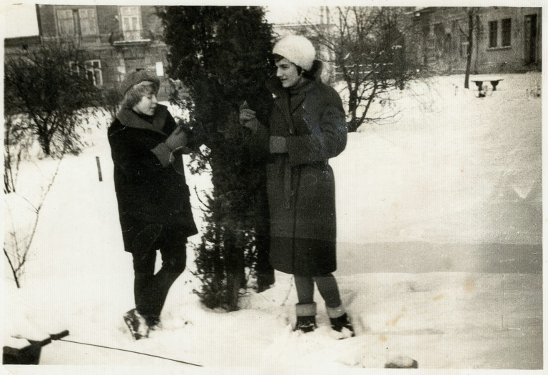 Siostry Irena (po mężu Miazga) i Janina Ozgówny pozują zimą do zdjęcia obok drzewa na plantach w Głogowie. W tle budynki północno – wschodniego narożnika Rynku.