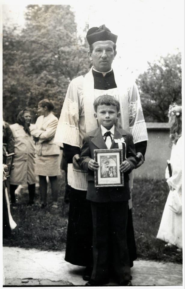 Chłopiec pozuje do pamiątkowego zdjęcia z okazji I Komunii Św. w Przewrotnem wraz z ks. Tadeuszem Bukałą.