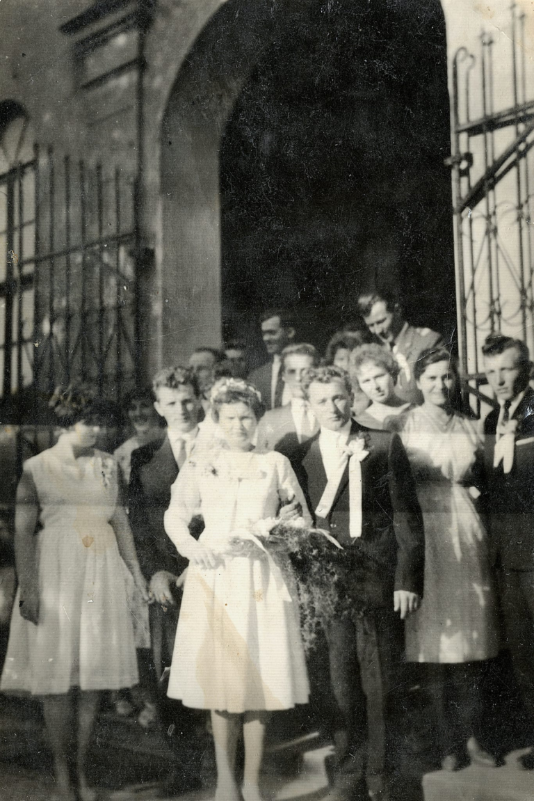 Państwo młodzi (p. Migutowie) wraz z gośćmi weselnymi pozują do zdjęcia przed wejściem do kościoła parafialnego w Głogowie.