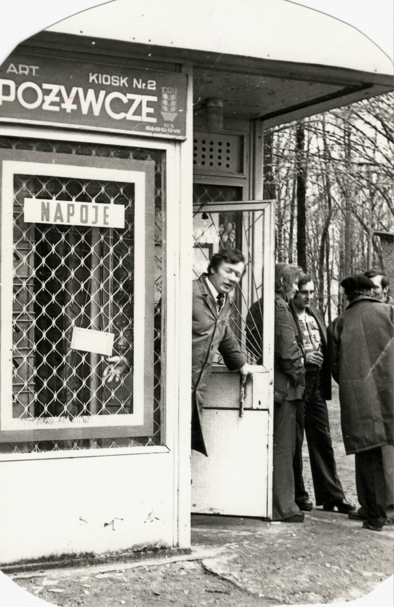 Pan Mieczysław Wszoła wychodzi z kiosku spożywczego w parku „Grabina”. Po jego prawej stronie stoi jeszcze czterech mężczyzn.