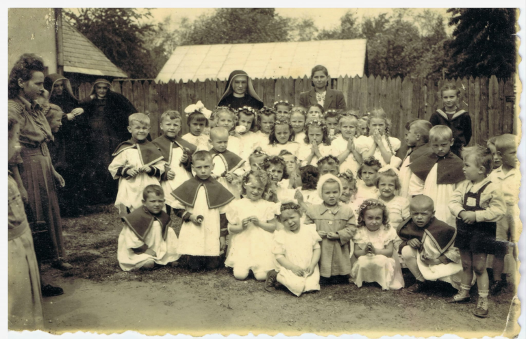 Grupa dzieci wraz z dorosłymi i zakonnicami pozuje do zdjęcia przed budynkiem ochronki w Głogowie po procesji Bożego Ciała.