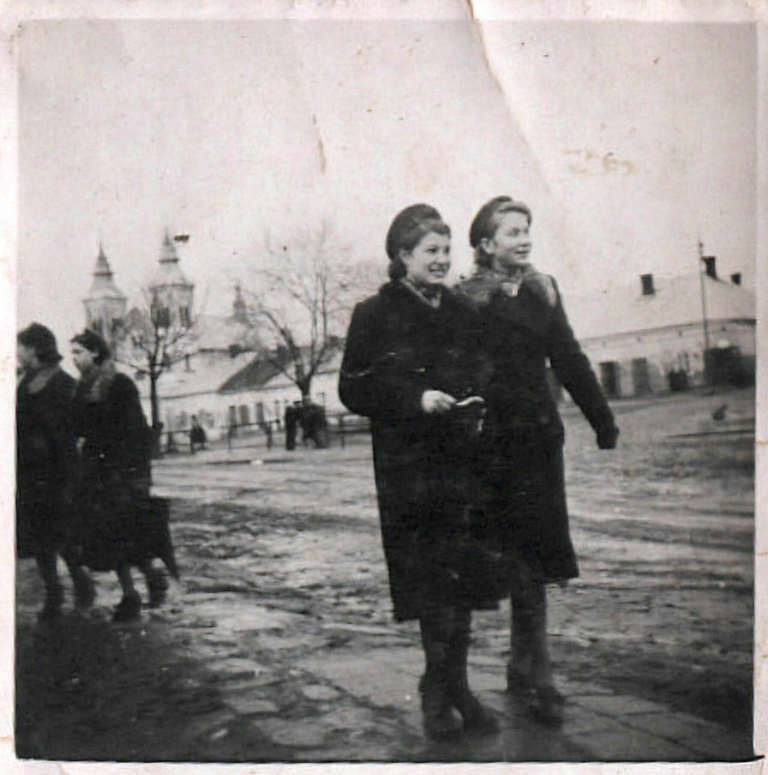 Dwie kobiety pozują do zdjęcia na Rynku w Głogowie. W tle od lewej kościół parafialny I domy od numeru 25 do 32.