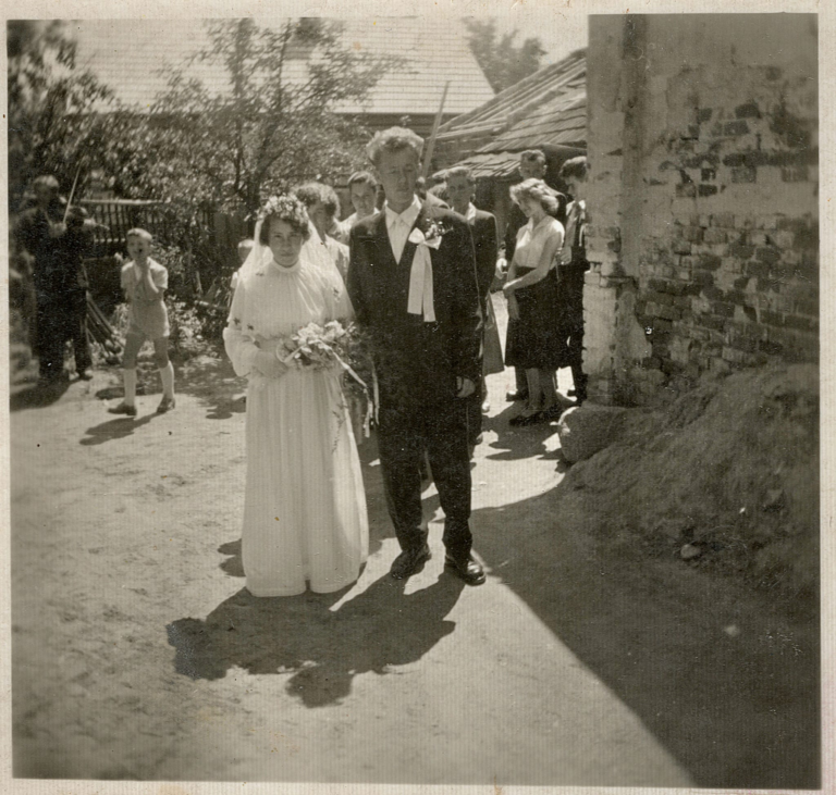 Państwo młodzi Maria i Mieczysław Wszołowie wychodzą ze swojego domu rodzinnego przy ulicy 3-go Maja w Głogowie w otoczeniu gości weselnych. W tle widoczny drewniany dom p. Rząsy przy ulicy Witosa.