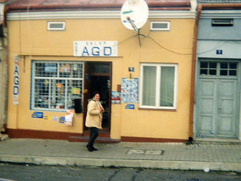 Domy nr 10 i 11 na głogowskim Rynku.Przed nr 10 stoi kobieta a nad drzwiami wisi szyld „Salon AGD”.