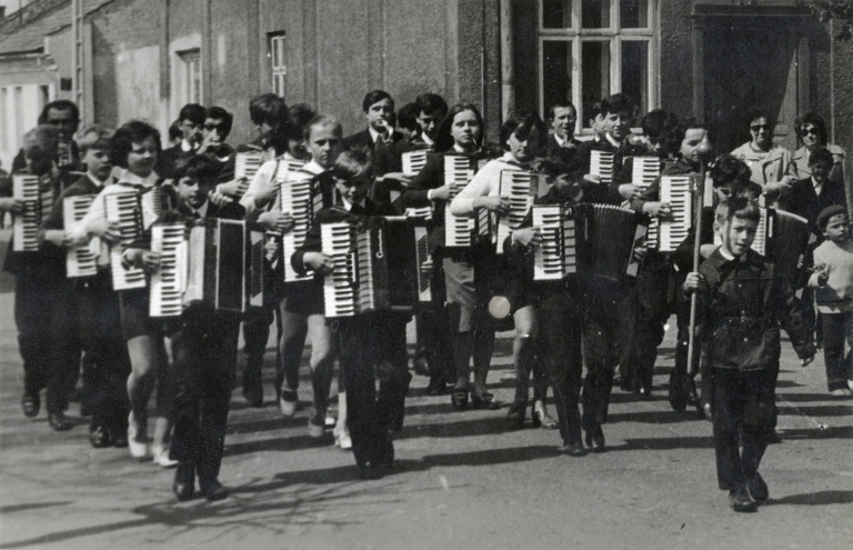 Orkiestra dziecięca na głogowskim Rynku w trakcie jednego z pochodów pierwszomajowych. W tle budynek Rynek nr 2 i 3-go Maja nr 2.